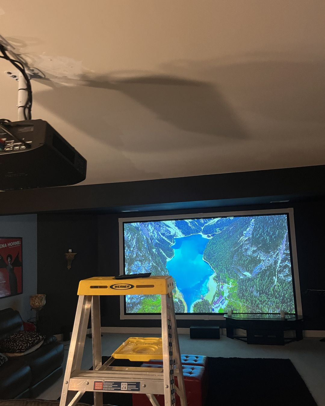 Ceiling-mounted projector on an extension pole being aligned to a large fixed-frame screen during the basement theater install