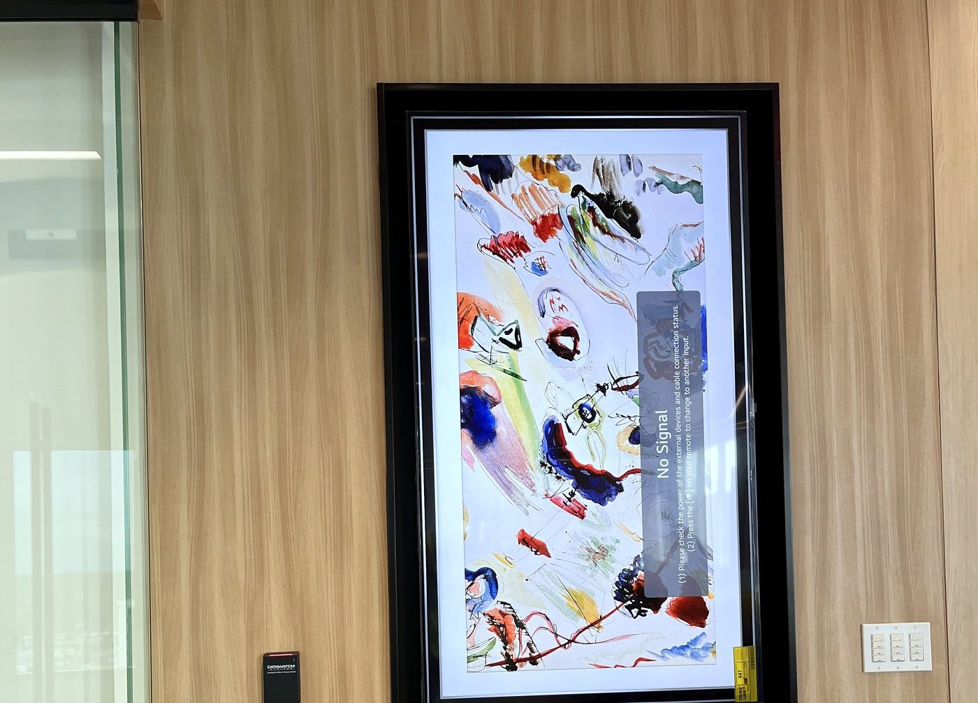 Framed gallery display flush-mounted on a wood feature wall with a wall keypad above
