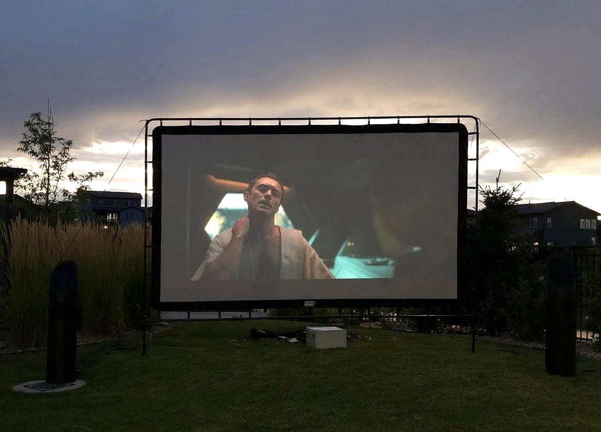 Outdoor projector screen and landscape speakers set up on a lawn at dusk