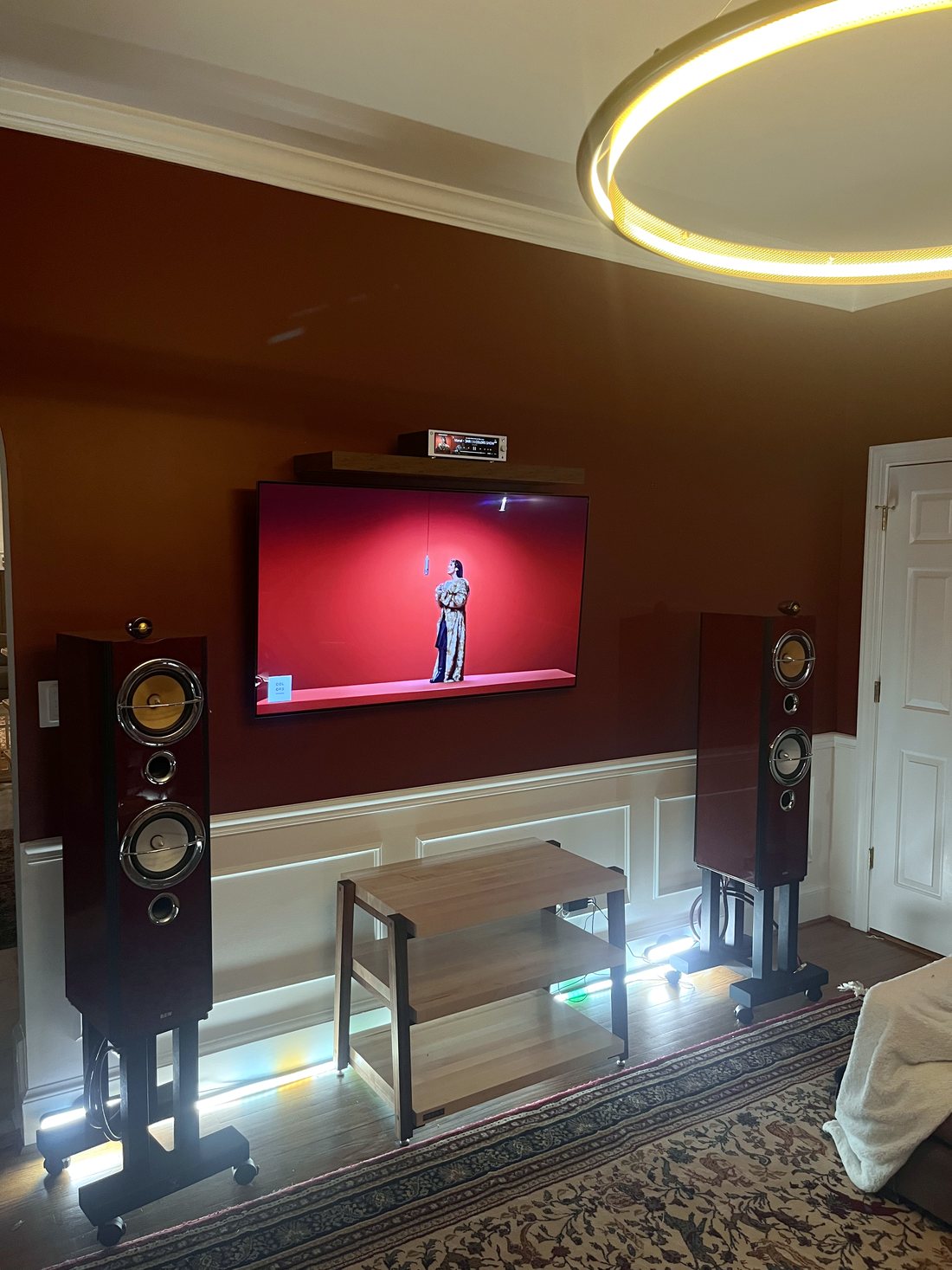 Finished living room install — wall-mounted TV flanked by floorstanding speakers over a lit media rack