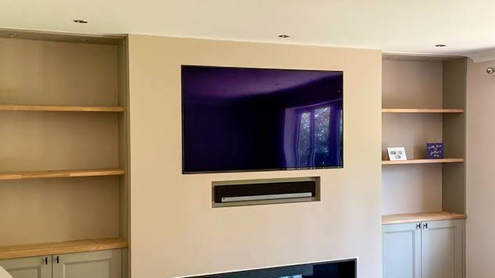 Built-in media wall with recessed TV, soundbar niche and linear electric fireplace flanked by shelving — Argos AV media wall installation