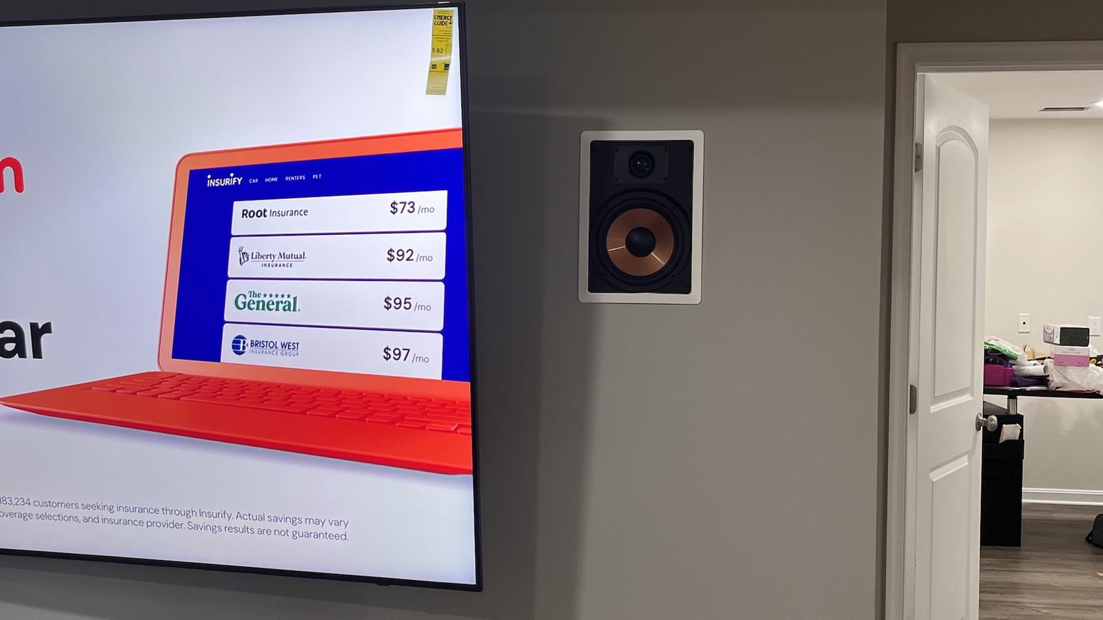 In-wall speaker installed flush beside a wall-mounted TV in a finished basement — Argos AV speaker wall mounting
